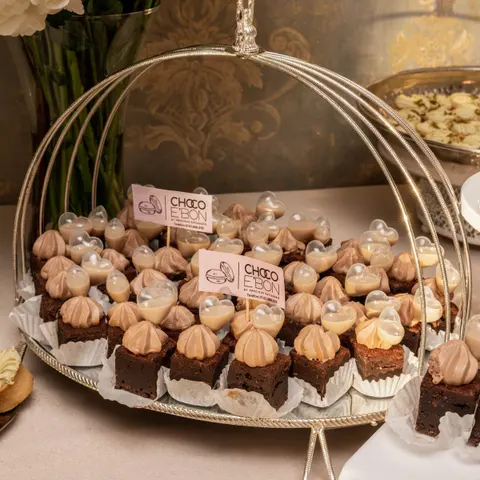 Brownies și prăjituri cu cremă sub un clopot argintiu, cu etichete Choco e'Bon