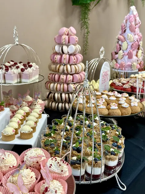 Candy bar cu două turnuri de macarons roz, cupcakes și pahare cu desert